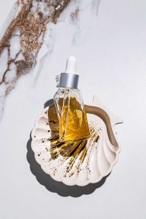 Glass dropper bottle with yellow liquid on a white shell against a marble background