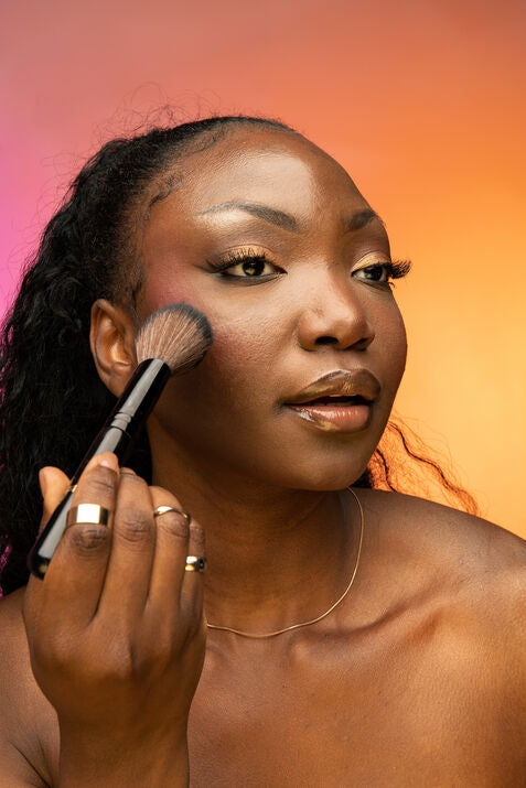 woman applying makeup against pink and orange backdrop