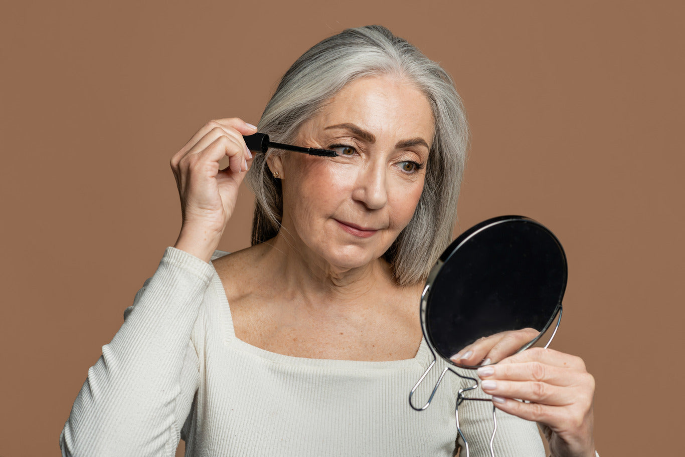 Older woman applying mascara using small mirror