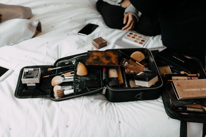 Makeup bag with makeup products and brushes on a bed