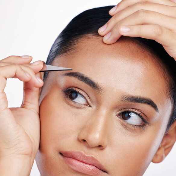 woman using tweezers to pluck her eyebrows