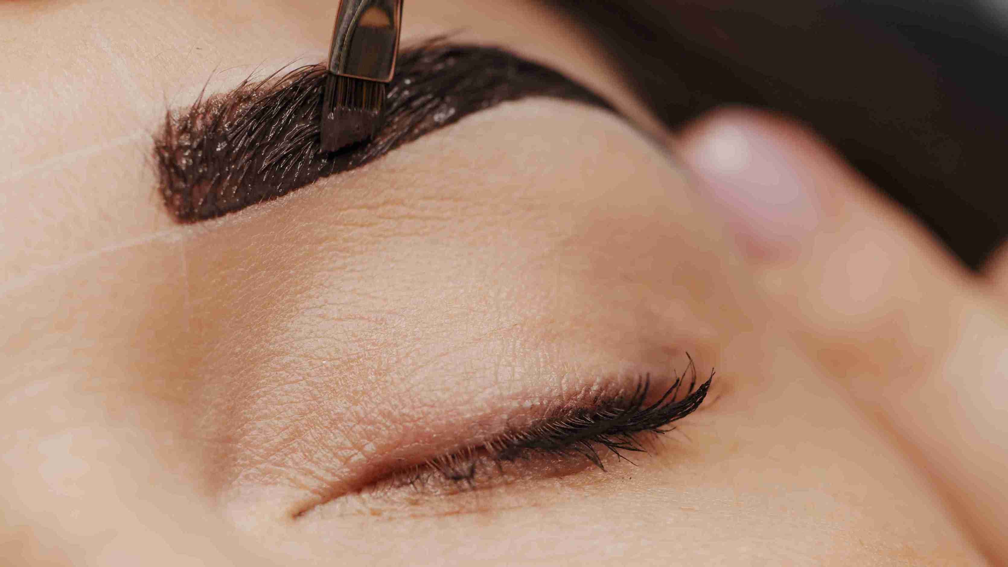 Eyebrow grooming with a brush on a close-up of an eye.