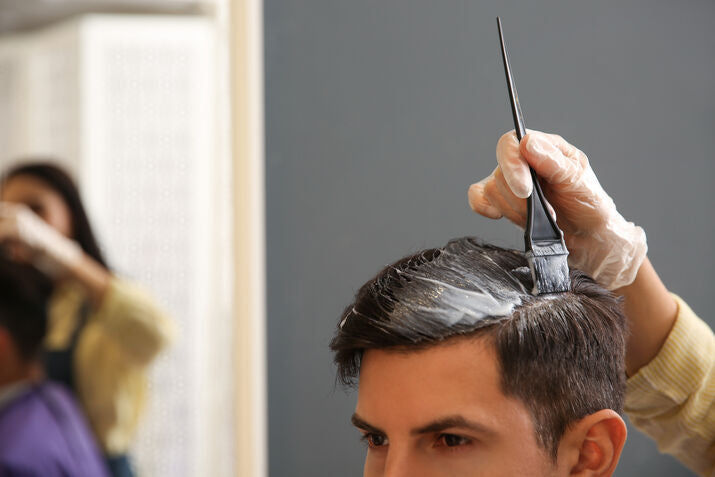 Person getting hair colored with a brush and dye, wearing gloves.