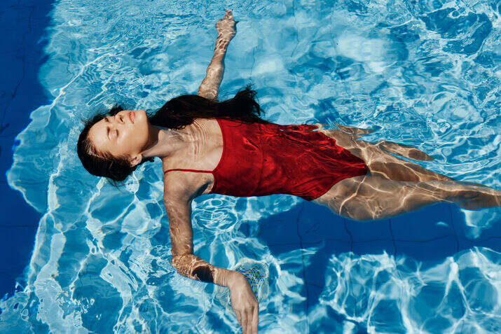 Woman in a red swimsuit floating in a pool with blue water.
