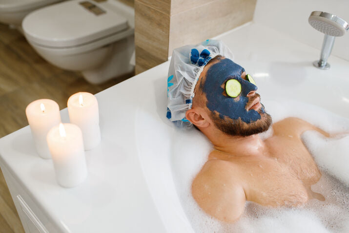 man relaxing in bath with face mask