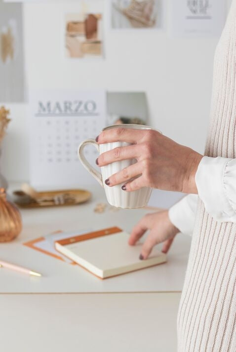 Woman with mug and hand reaching for notebook 