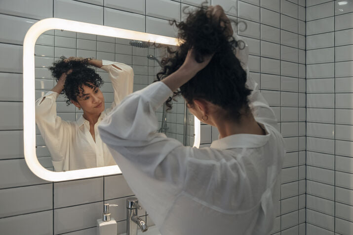 A woman with curly hair looking into a mirror as she styles she hair